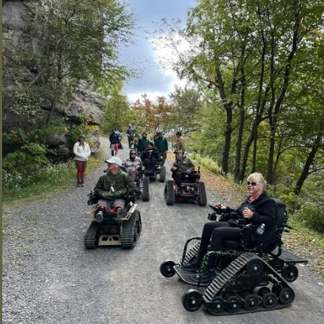 Several people in track chairs gather at a hiking trail.