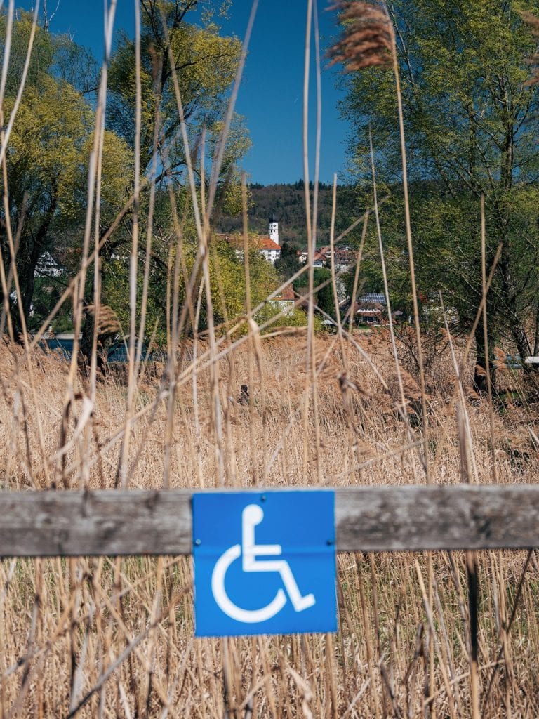 A handicapped sign is show on a wooden fence outdoors.