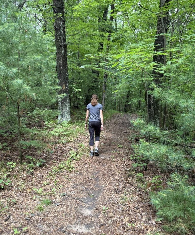 A woman walks in a trail with trees surrounding her.